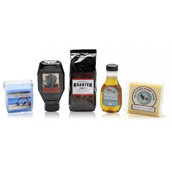 Įvairūs produktai ant baltos paviršiaus: plastikinė dėžutė su žuvies paveikslu, juodas laikrodis, kavos pakelis, agavų nektaro buteliukas ir sūris supakuotas į popierių.