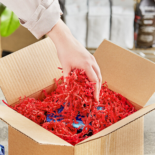 Rankų gestas įdėti arba išimti daiktą iš kartoninės dėžės, užpildytos raudonos spalvos pakavimo šiaudeliais.
